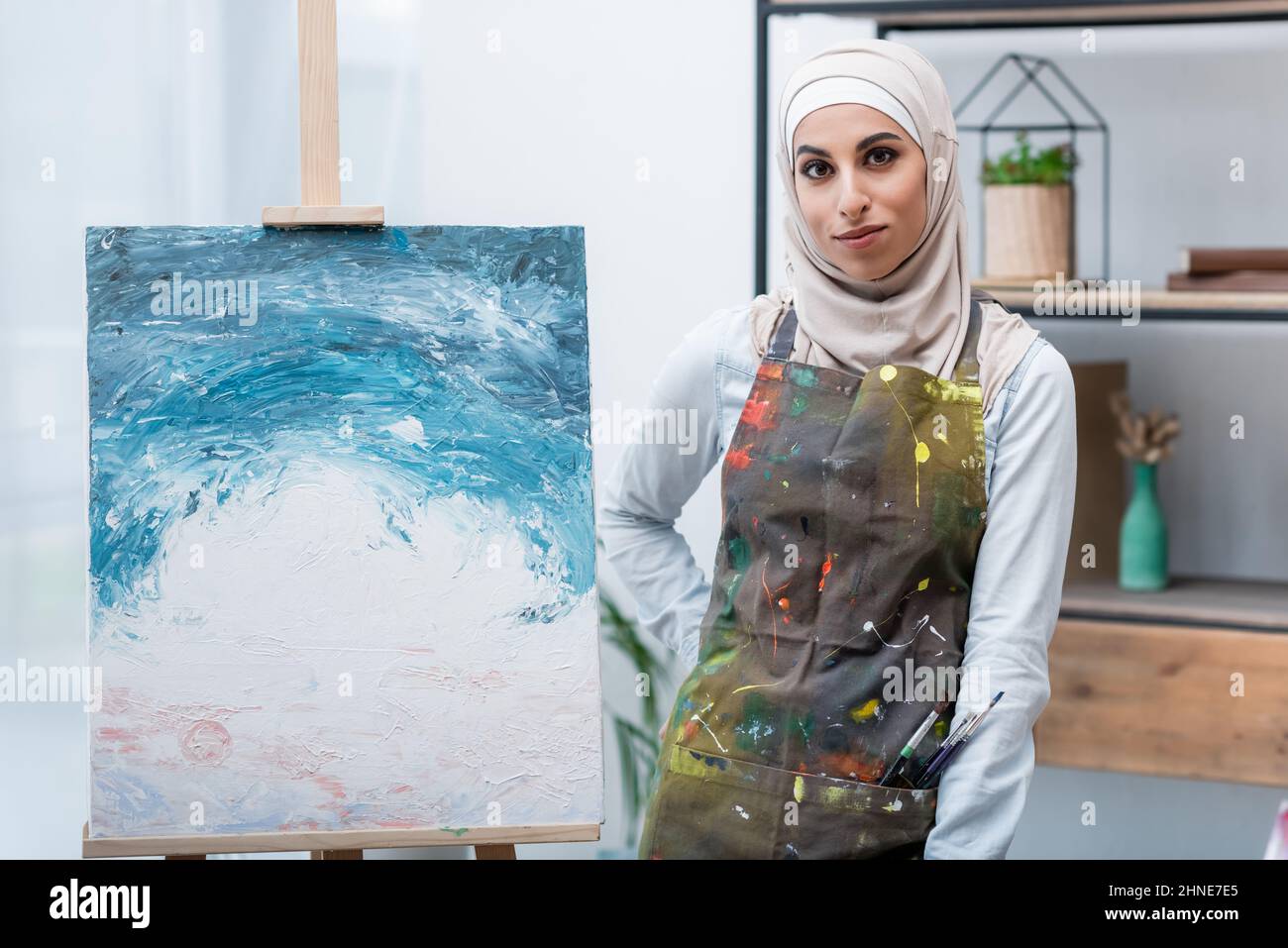 femme musulmane regardant la caméra tout en se tenant de la main sur la hanche près de la peinture Banque D'Images