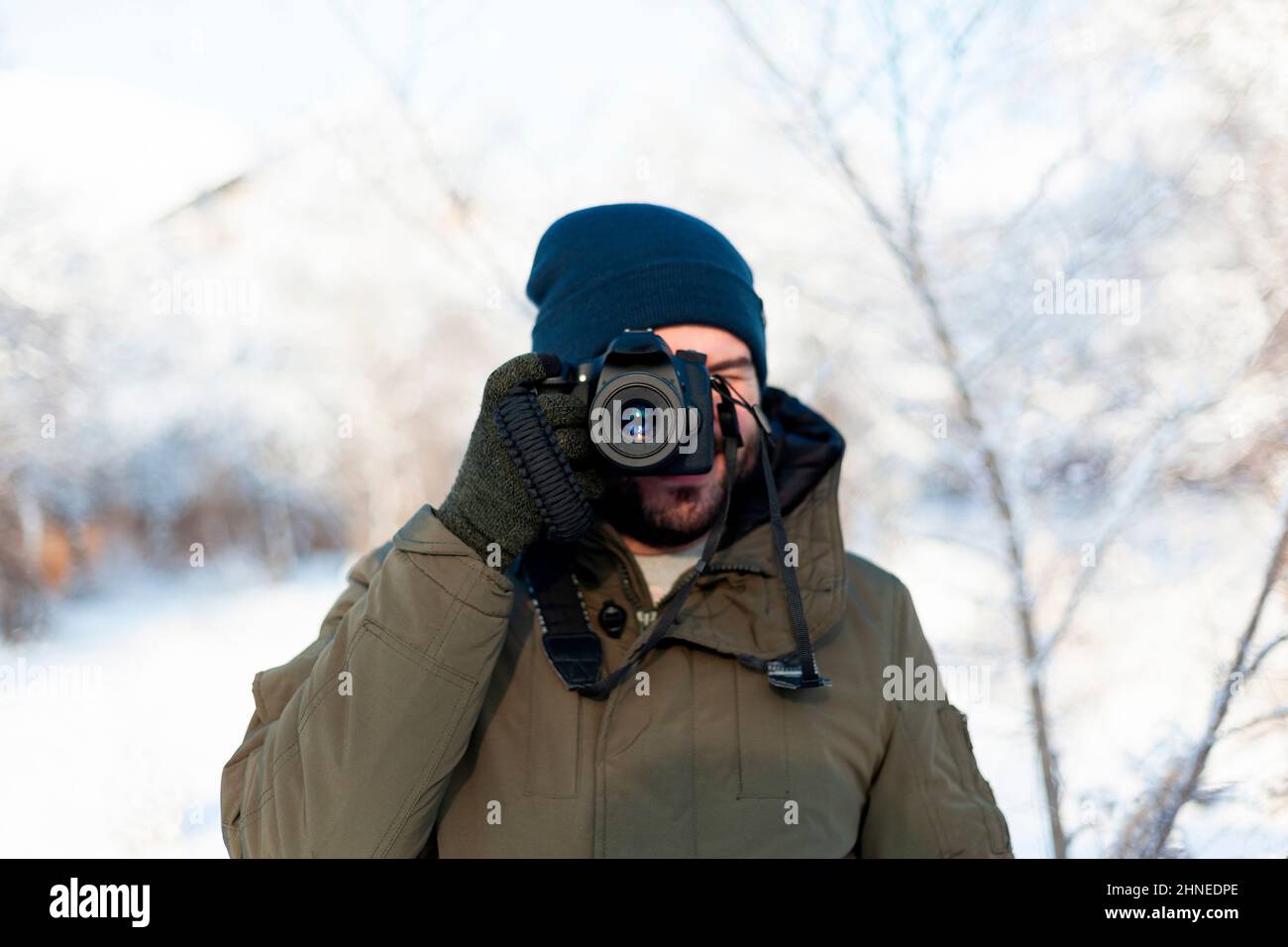 Un homme dans un chapeau d'hiver et des mitaines filme avec un appareil photo reflex numérique tout en se tenant debout à l'extérieur Banque D'Images