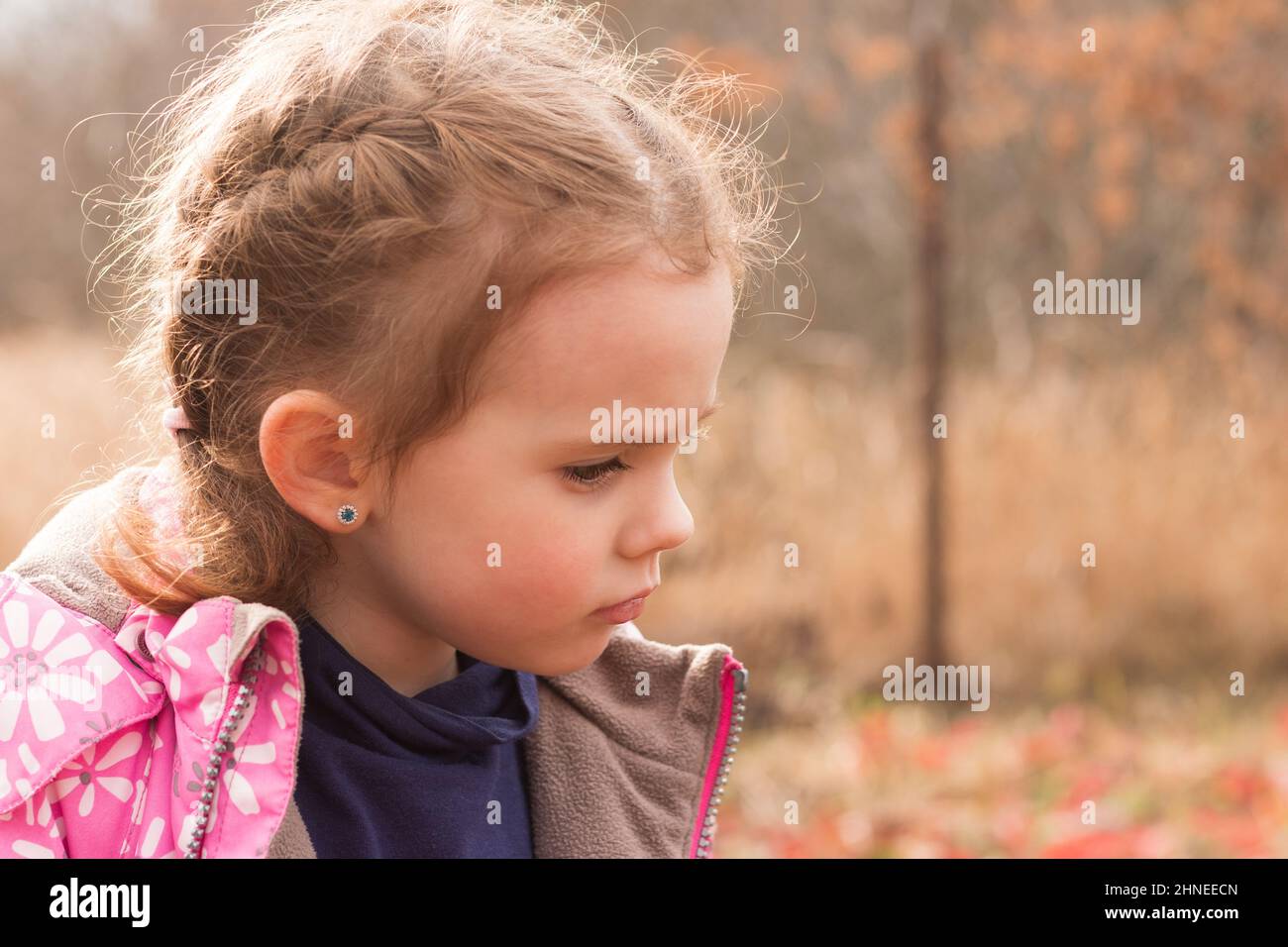 Petite belle jolie petite fille triste dans une veste avec des cheveux blonds en queue de porc se tient sur un fond d'automne Banque D'Images