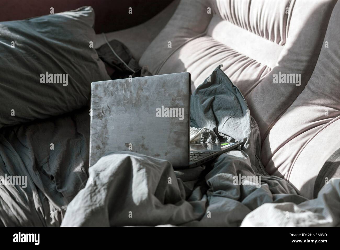 un ordinateur portable avec des empreintes digitales dans un lit désordonné, coup de lumière du matin Banque D'Images
