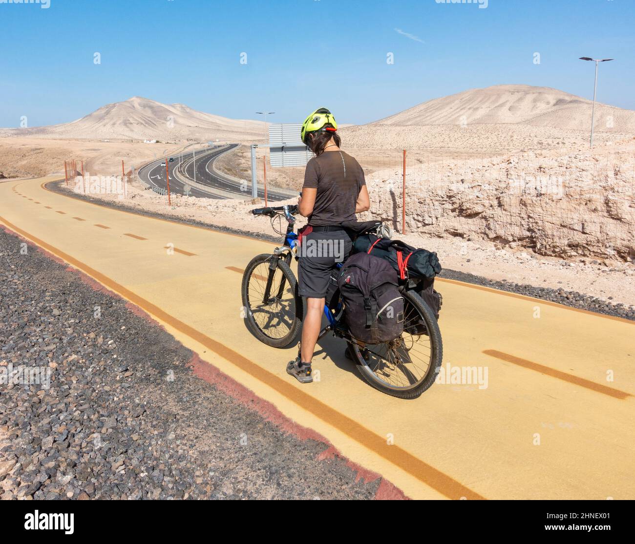 Femme cycliste visitant les îles Canaries sur un sentier cyclable désigné à côté de la route très fréquentée sur la côte est de Fuerteventura, îles Canaries, Espagne Banque D'Images