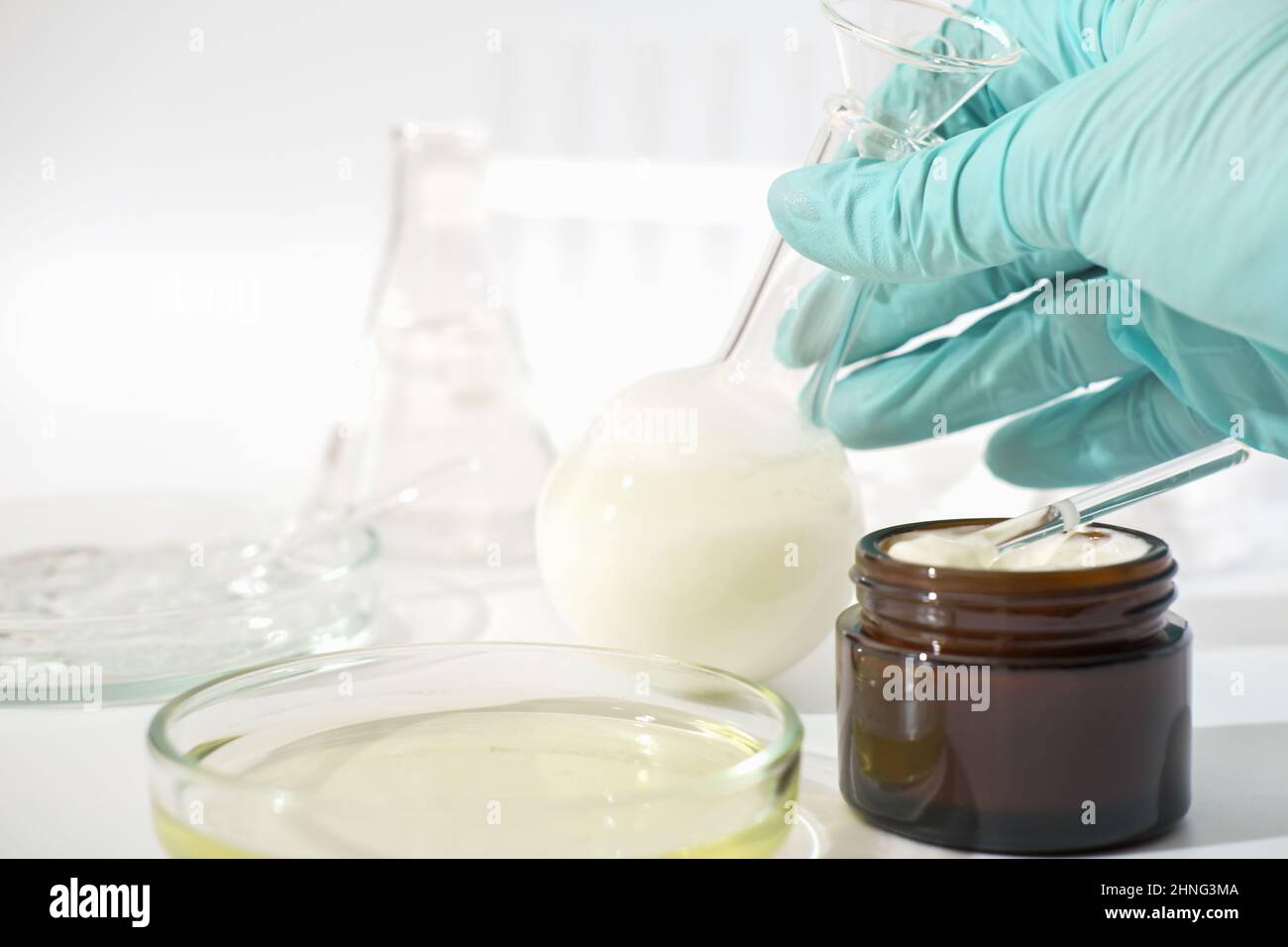 main dans le gant médical en caoutchouc contenant la verrerie de laboratoire avec produit cosmétique fermenté, crème visage avec enzymes développée dans un laboratoire Banque D'Images