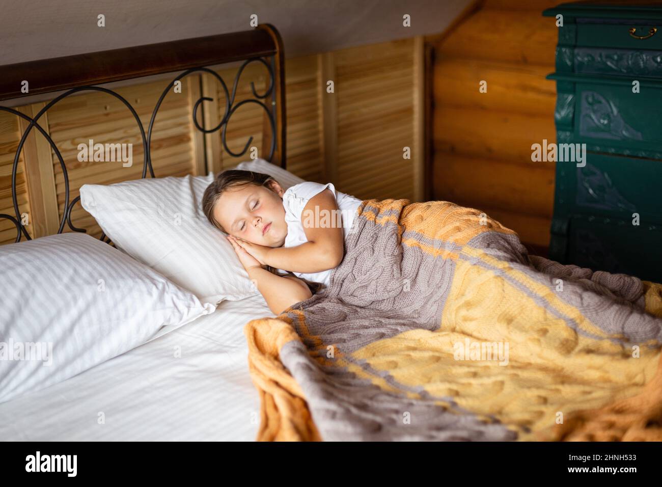 Jeune fille caucasienne prenant la sieste sur un grand lit double avec les  deux mains sous la tête recouverte d'une couverture avec la poitrine des  tiroirs derrière le lit dans une maison