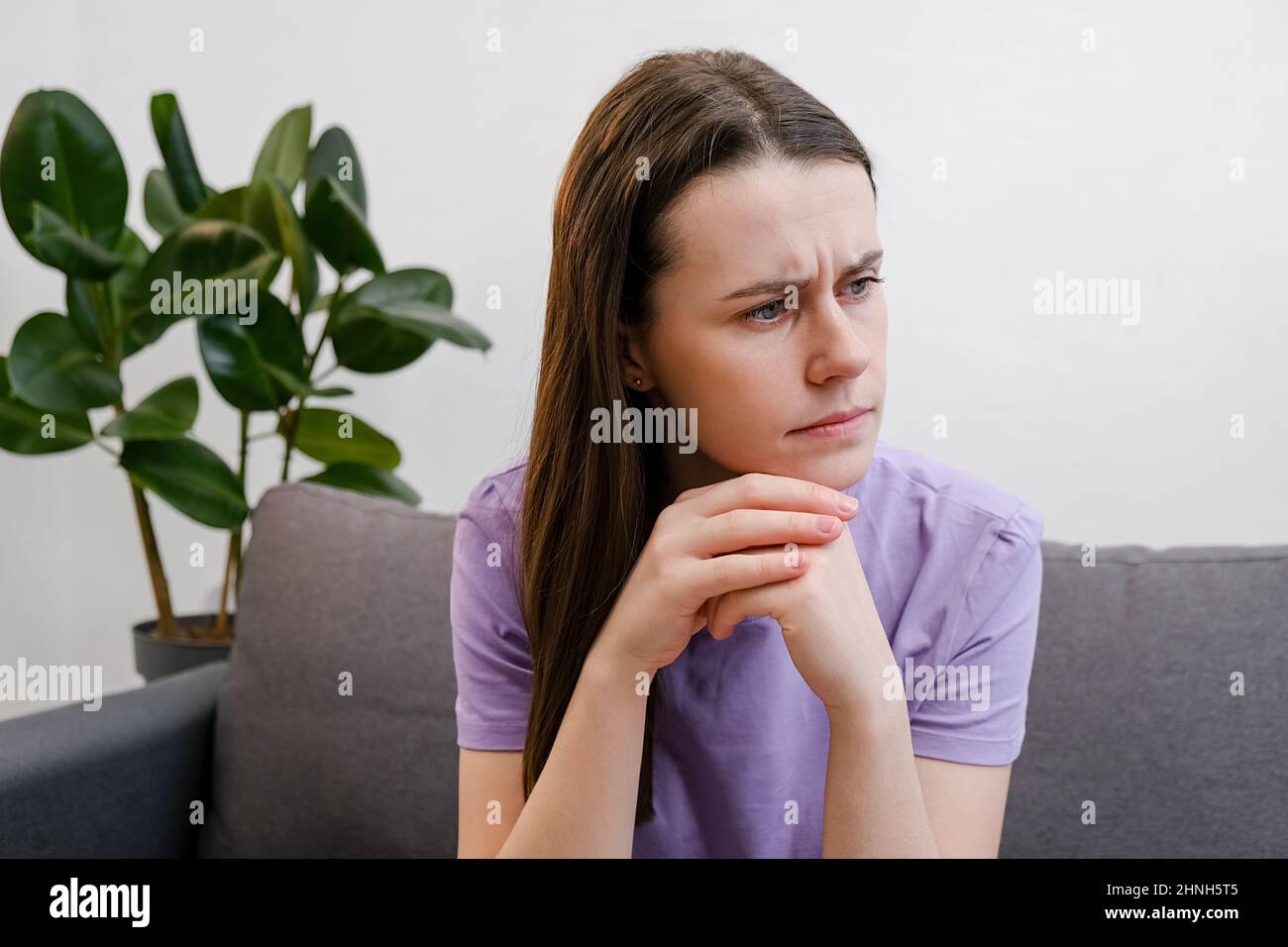 La jeune femme pensive 20s ans pense aux problèmes personnels ou de relations, regarde dans la distance se sent réfléchie s'occupant assis sur le canapé seul à li Banque D'Images