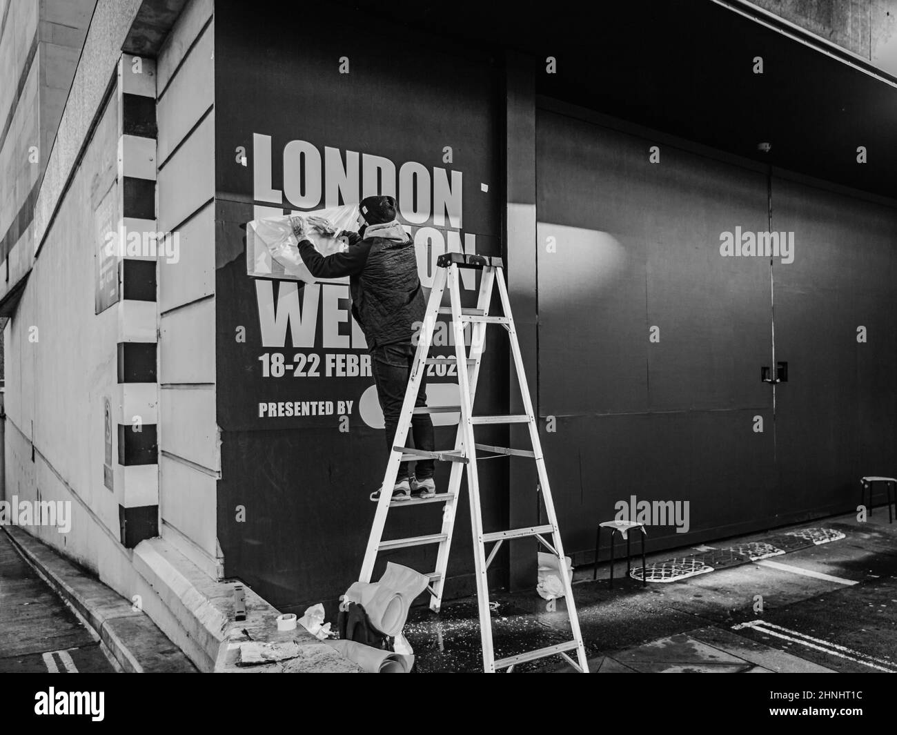 Une image en noir et blanc d'un homme mettant un panneau pour le début de la semaine de mode de Londres. Banque D'Images