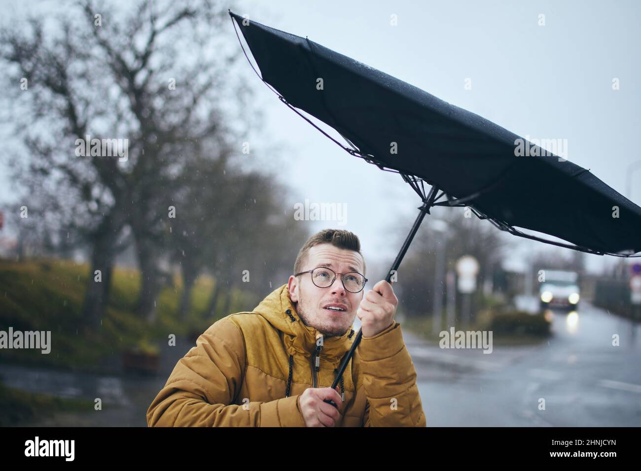 Homme tenant un parapluie cassé dans un vent fort pendant une sombre journée de pluie. Thèmes météo, météorogie et changements climatiques. Banque D'Images