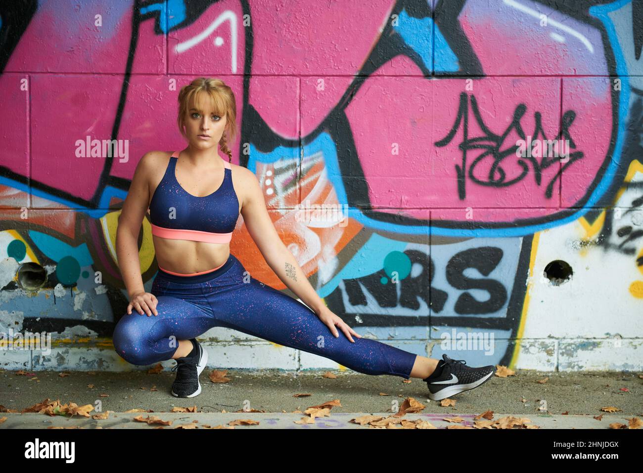 Jeune femme blonde à yeux bleus s'entraînant et s'exerçant à l'extérieur en portant un soutien-gorge de sport et des leggings Banque D'Images