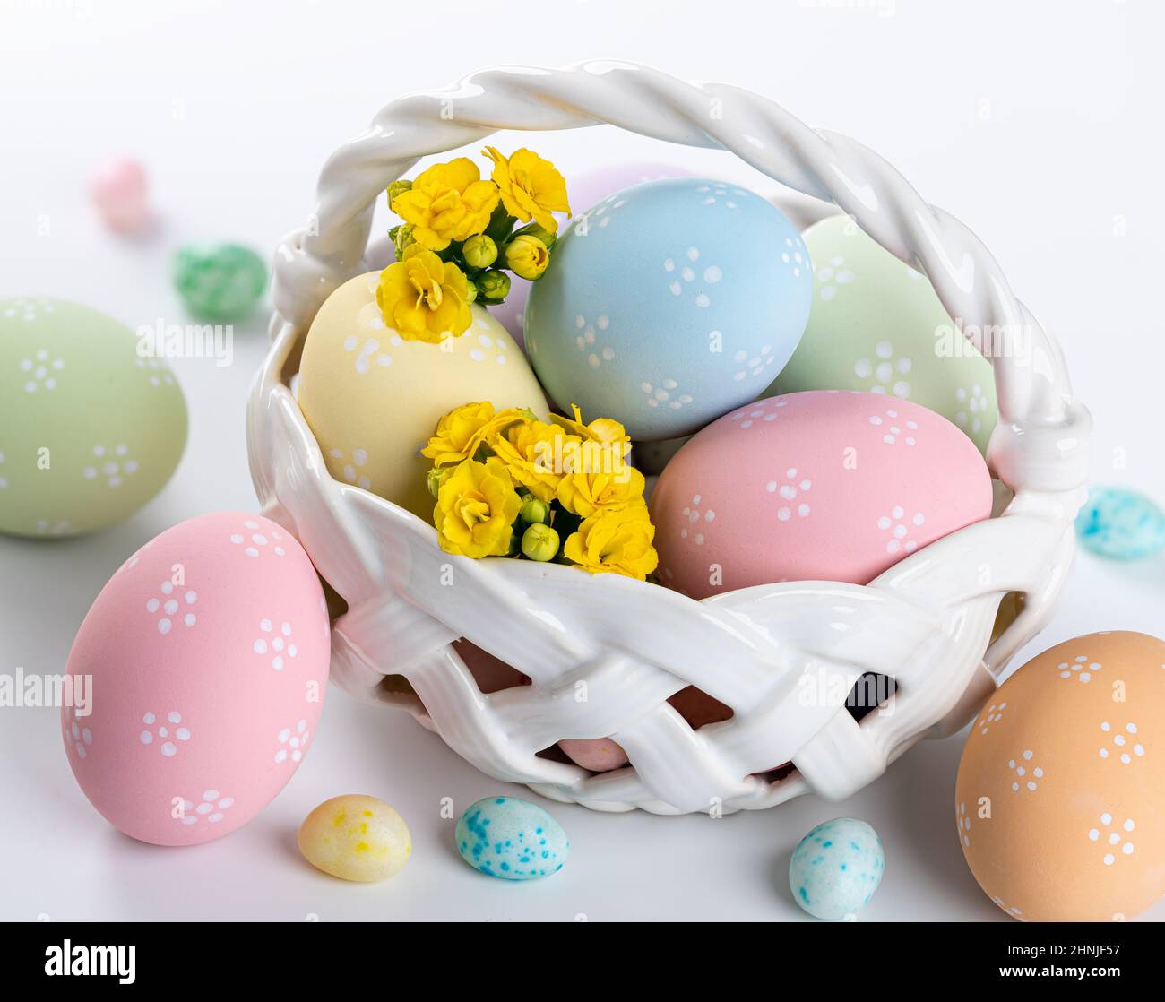 Œufs de pâques colorés, fleurs jaunes et bonbons dans un panier et sur fond blanc Banque D'Images