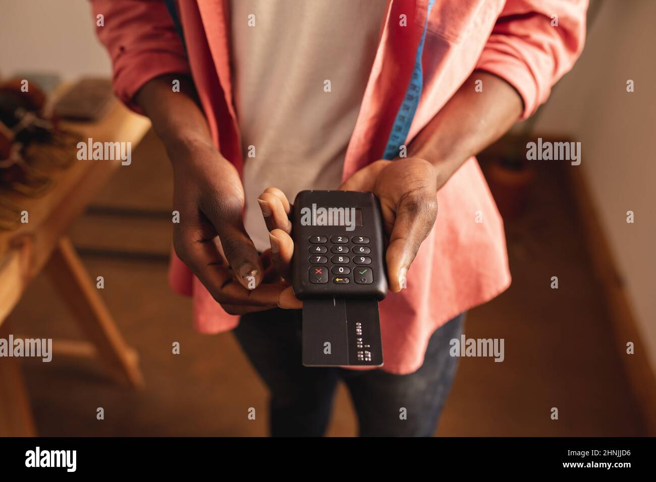Section médiane de jeune homme afro-américain tenant une machine de lecteur de carte de crédit dans une petite boutique Banque D'Images
