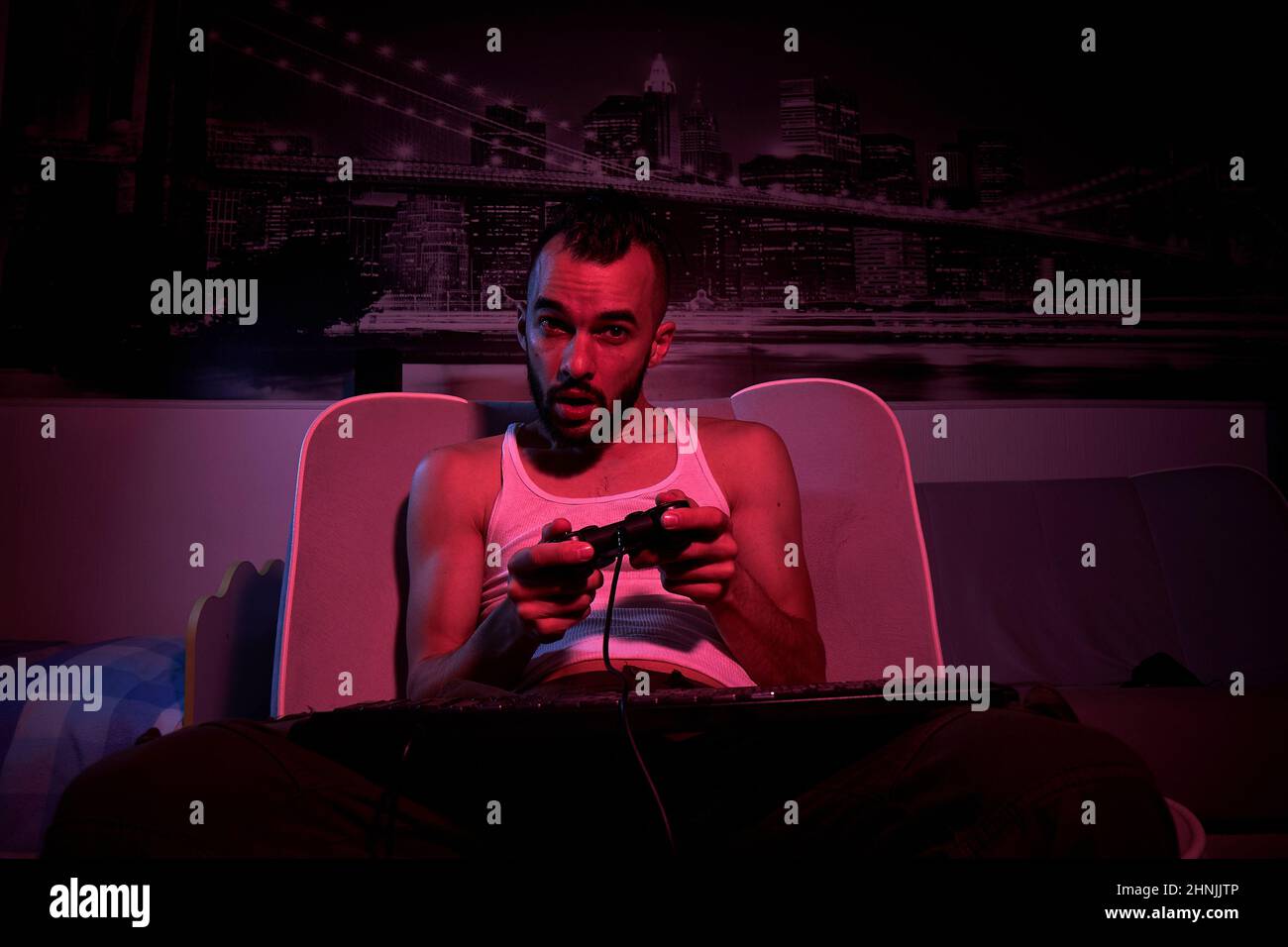 un garçon de trente ans avec un joystick dans ses mains joue à des jeux d'ordinateur, éprouvant diverses émotions. assis sur le canapé à la maison. vue de t Banque D'Images