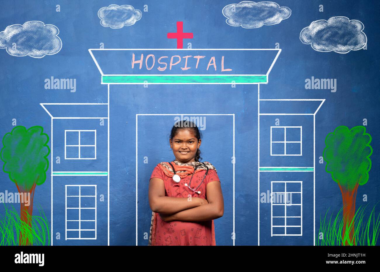 Joyeux sourire jeune fille indienne avec stéthoscope debout devant la peinture de l'hôpital - concept de pauvre enfant rêvant sur le médecin comme carrière future Banque D'Images