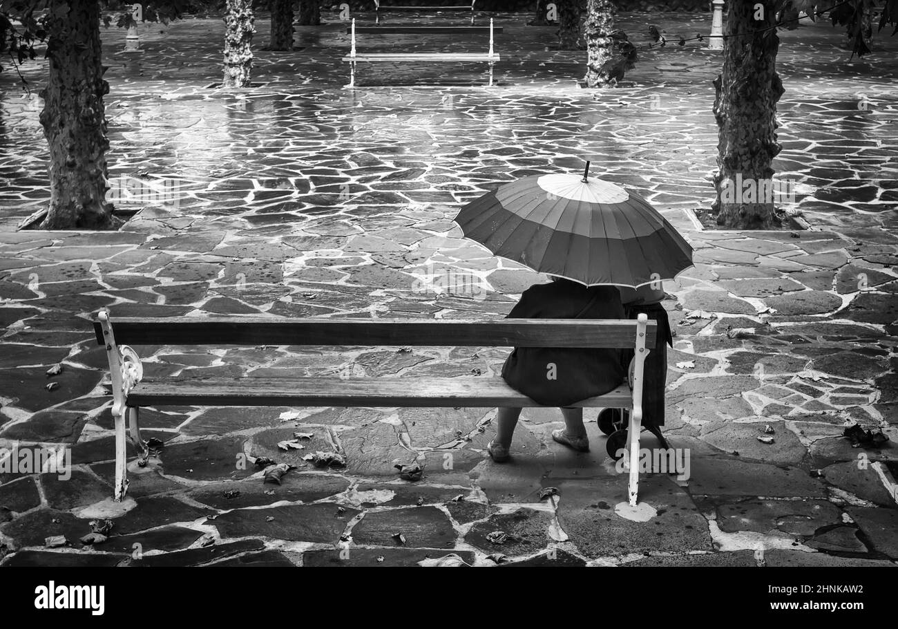 Femme âgée assise avec un parapluie Banque D'Images