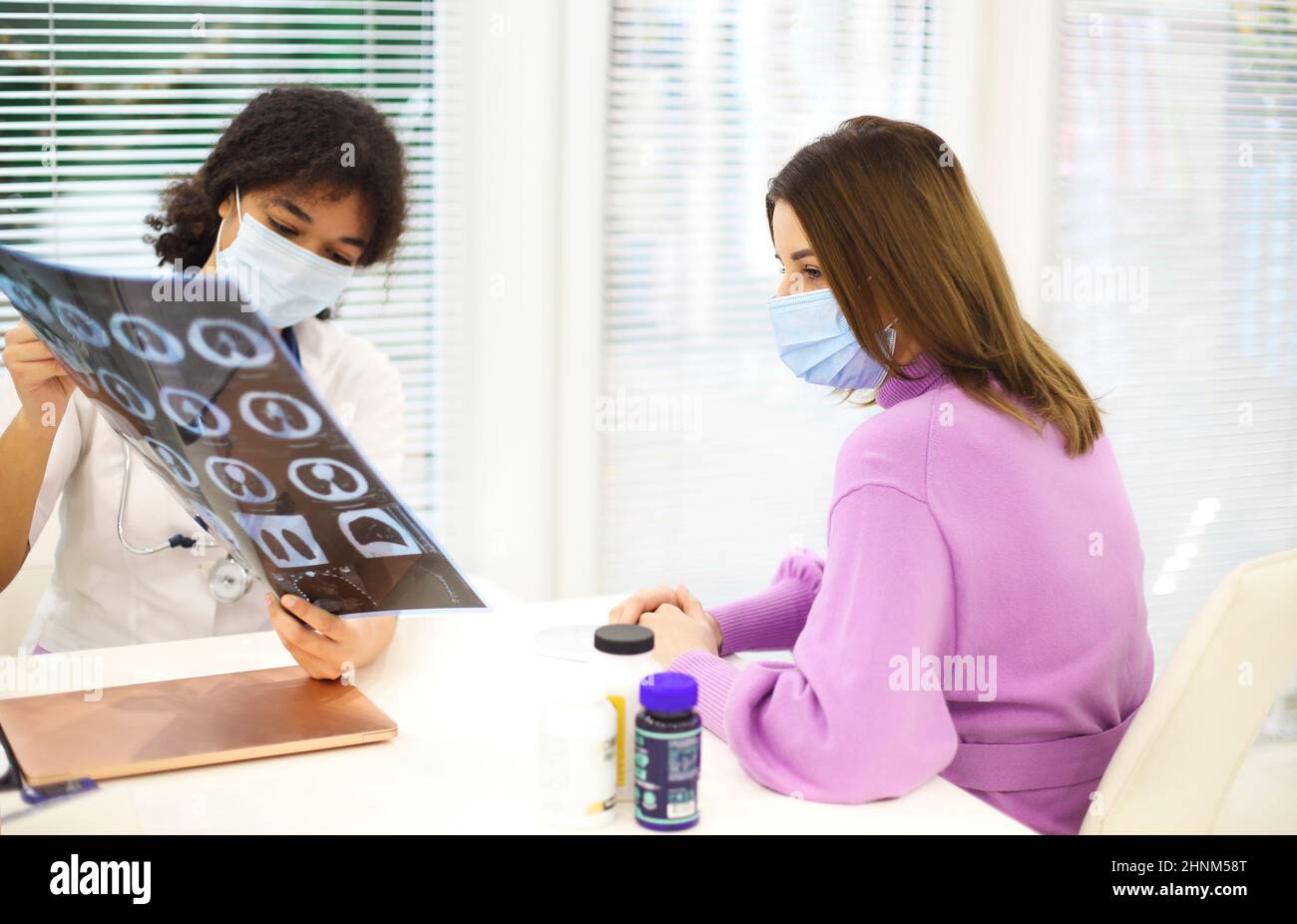 Le médecin et le patient qui se trouvent dans un masque facial de protection discutent du résultat des rayons X pendant le rendez-vous. Femme afro-américaine médecin avec TDM de dépistage pulmonaire extrainin Banque D'Images