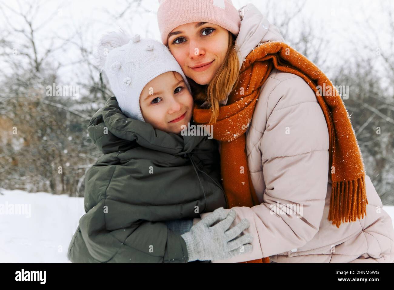 Belle famille heureuse mère et petite fille s'amuser par temps neigeux à l'extérieur, joyeuse maman ludique avec enfant embrassant tout en passant du temps ac Banque D'Images