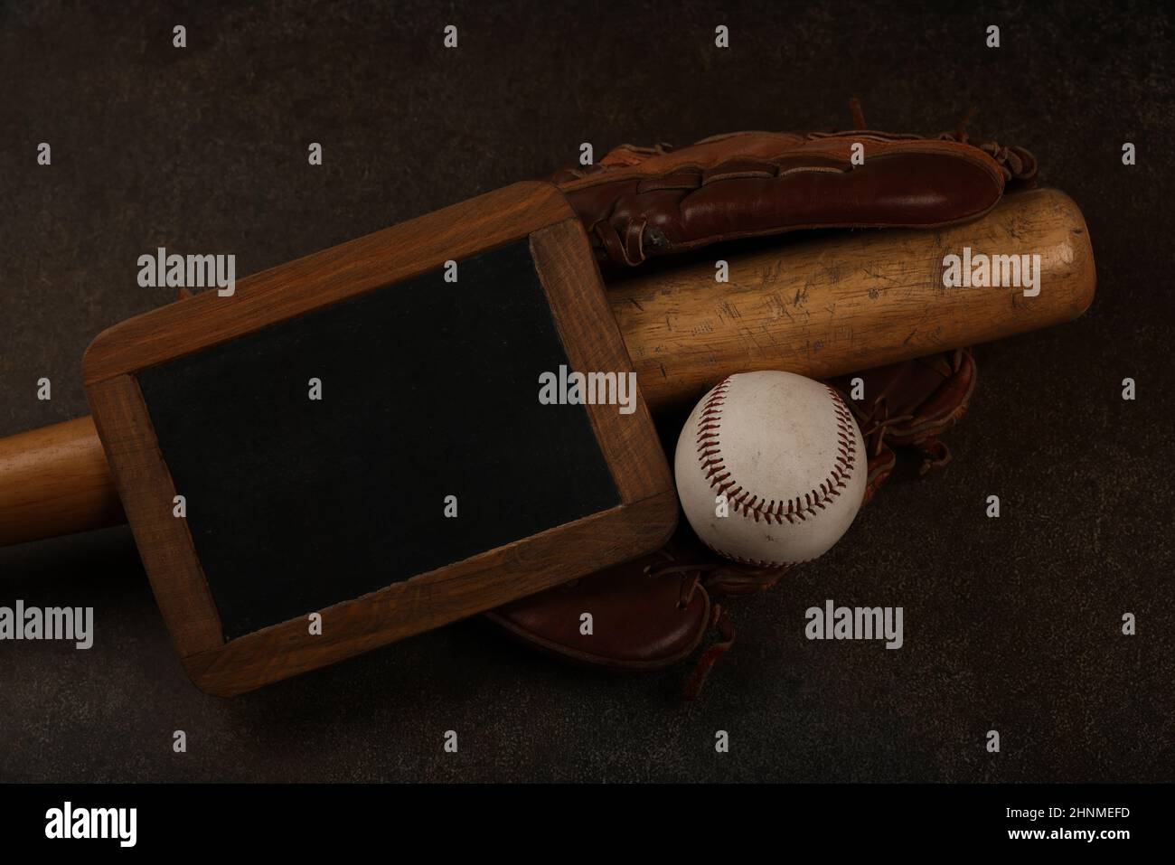 Gros plan sur une vieille balle de baseball, une bate en bois, un gant de cuir vintage porté et un panneau noir sur fond brun foncé grunge, vue du dessus en hauteur, direct Banque D'Images