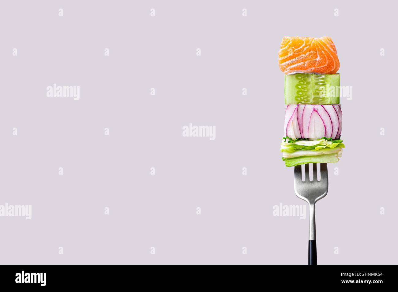 fourchette avec nourriture sur elle: délicieux filet de saumon, concombre, oignon, salade sur fond gris Banque D'Images