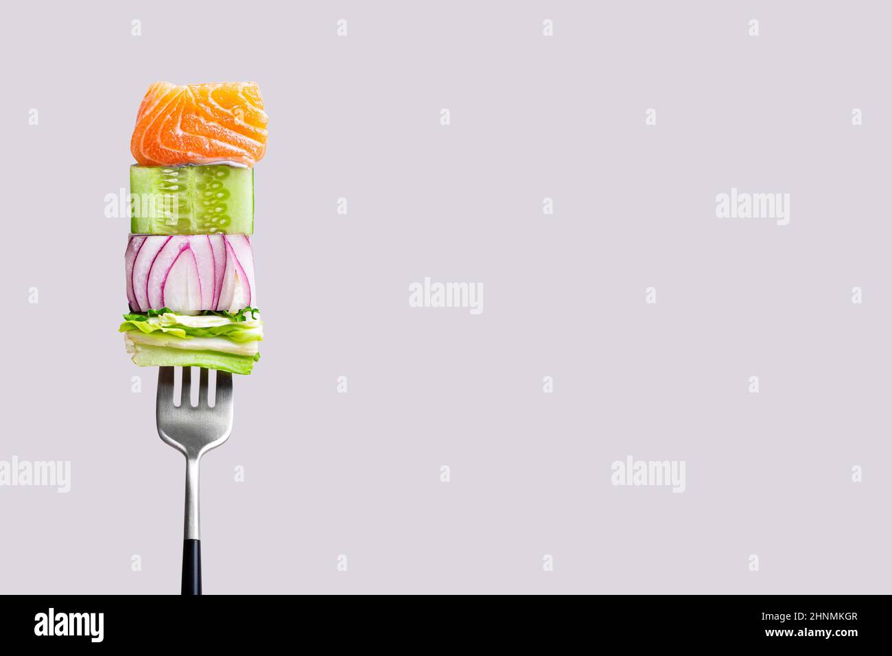 fourchette avec nourriture sur elle: délicieux filet de saumon, concombre, oignon, salade sur fond gris Banque D'Images