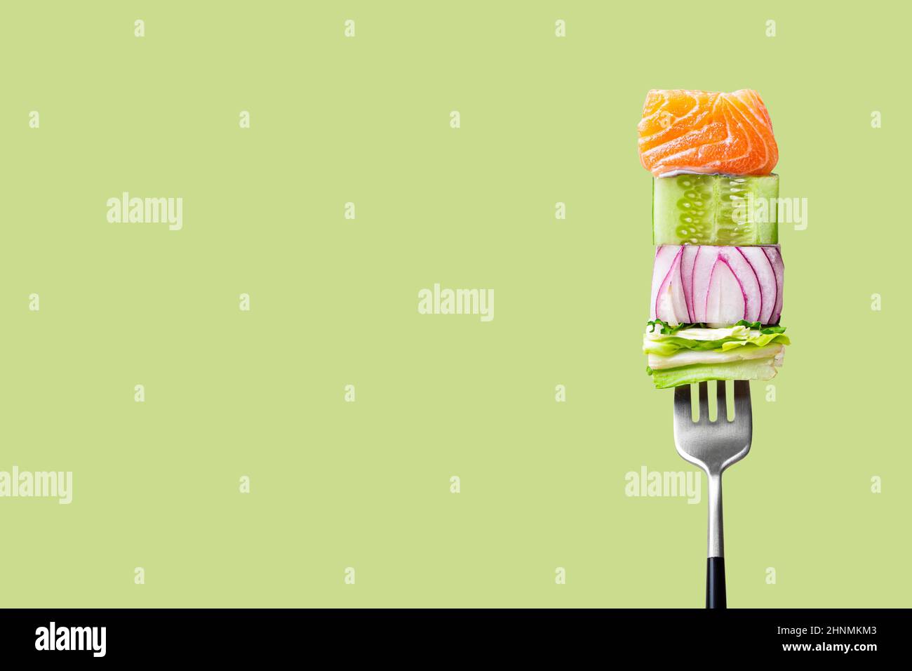 fourchette avec nourriture sur elle: délicieux filet de saumon, concombre, oignon, salade sur fond vert Banque D'Images