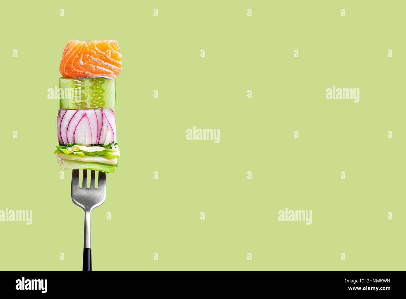 fourchette avec nourriture sur elle: délicieux filet de saumon, concombre, oignon, salade sur fond vert Banque D'Images