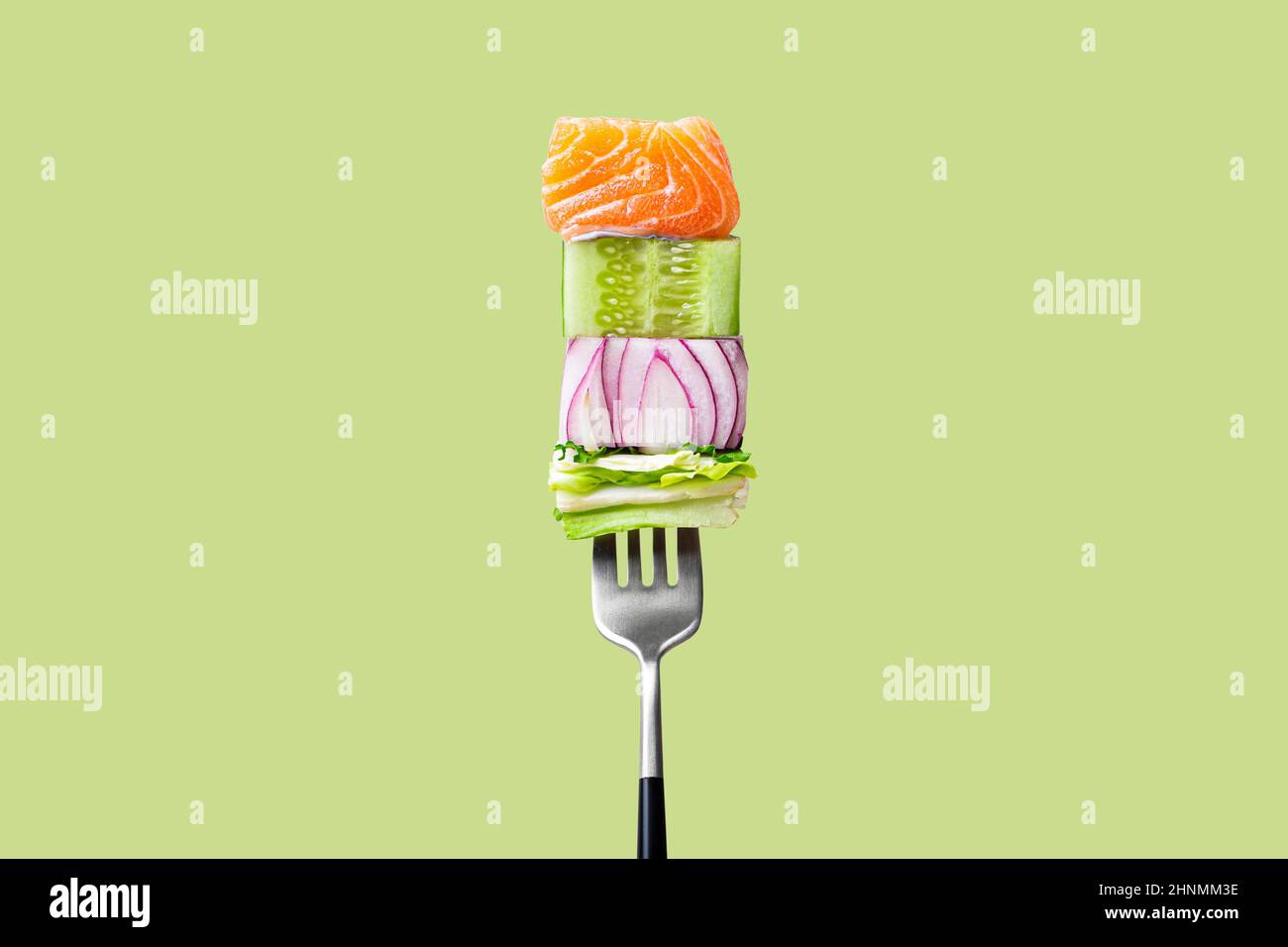 Gros plan de la fourchette avec la nourriture dessus: Délicieux filet de saumon, concombre, oignon, salade sur fond vert Banque D'Images