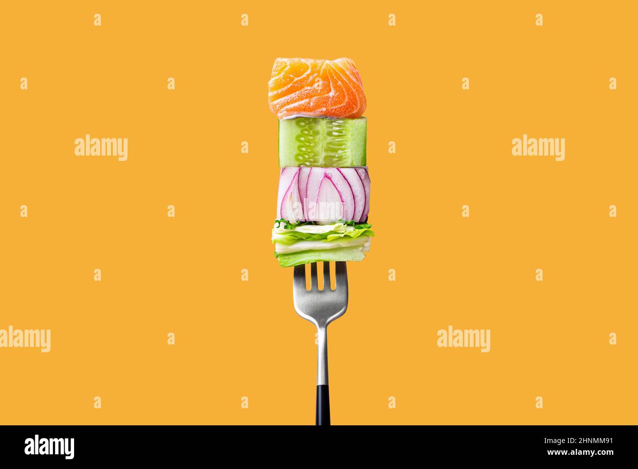 fourchette avec nourriture sur elle: délicieux filet de saumon, concombre, oignon, salade verte sur fond orange Banque D'Images
