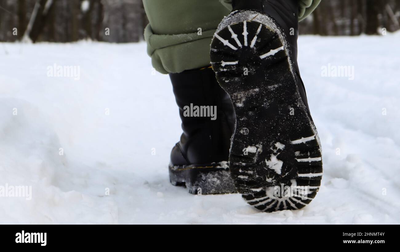 Jambes de femme en bottes noires, marche d'hiver dans la neige. Femme active marchant loin de la caméra dans la forêt d'hiver. Concentrez-vous sur vos jambes. Beau temps d'hiver blanc avec des chutes de neige fraîches. Banque D'Images