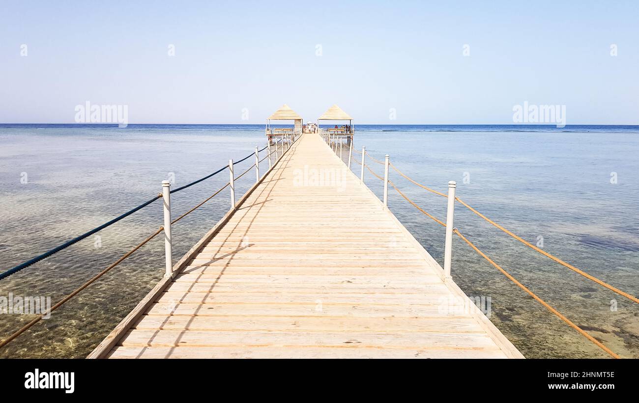Long ponton sur la mer Rouge en Égypte. Ponton pour la descente dans l'eau. Pont en bois sur le territoire de l'hôtel Amway à Sharm El Sheikh avec des clôtures métalliques et une corde au-dessus de la mer avec des vagues Banque D'Images