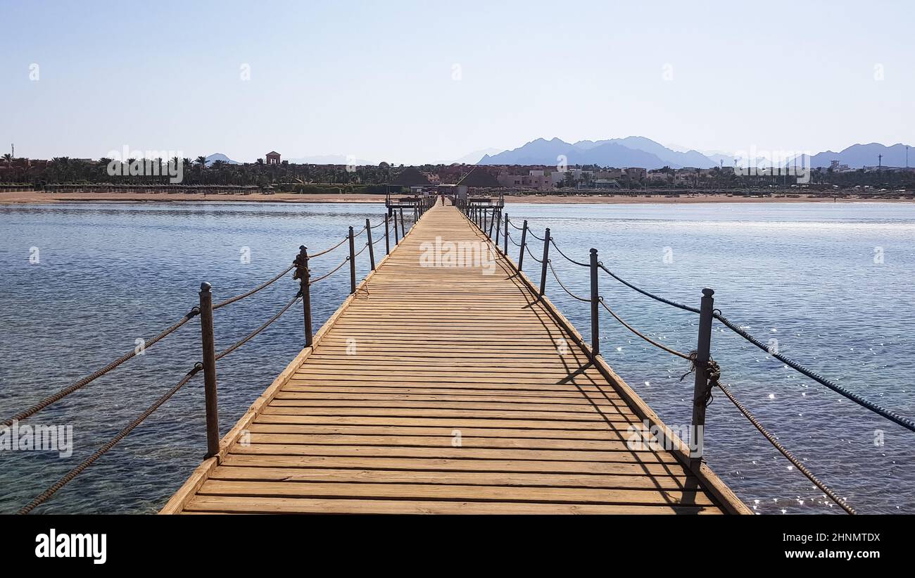 Long ponton sur la mer Rouge en Égypte. Ponton pour la descente dans l'eau. Pont en bois sur le territoire de l'hôtel Amway à Sharm El Sheikh avec des clôtures métalliques et une corde au-dessus de la mer avec des vagues Banque D'Images