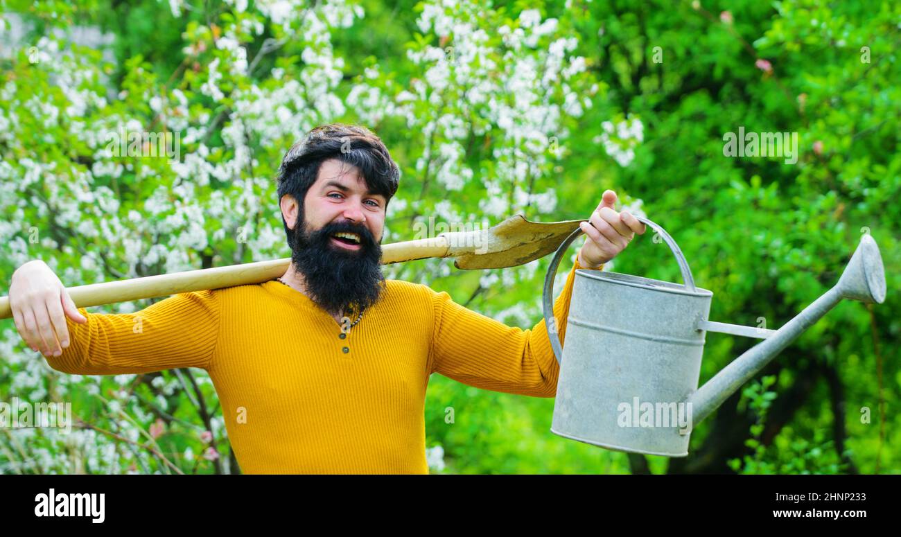 Jardinier barbu avec arrosoir et bêche se préparant à la plantation. Agriculteur travaillant dans le jardin de printemps. Banque D'Images