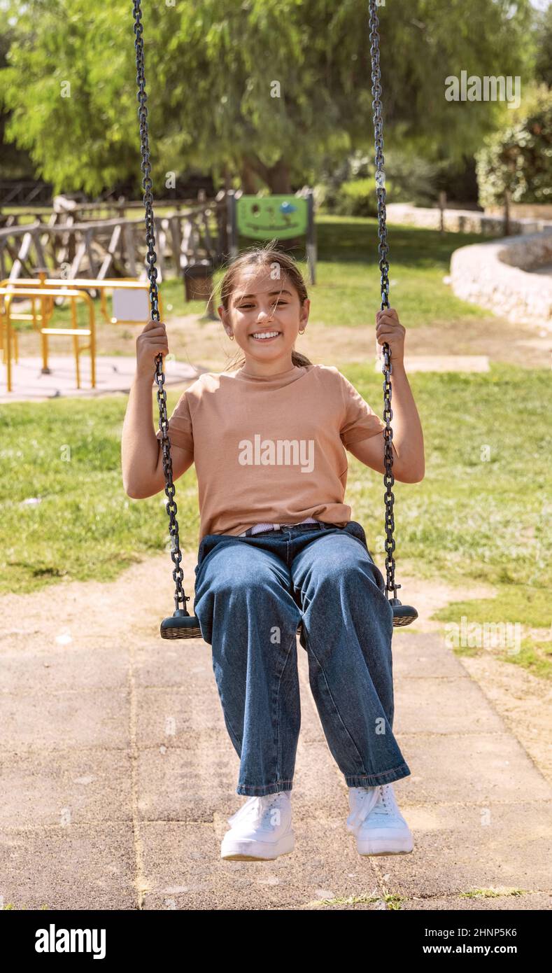 Bonne fille d'enfant s'amuser avec balançoire à chaîne sur le terrain de jeu dans un parc Banque D'Images