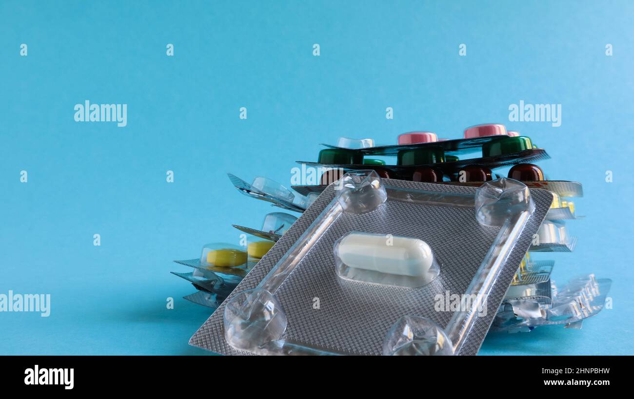 Des paquets de pilules de différentes formes et couleurs sont empilés sur un fond bleu. Les gélules sont conditionnées en plaquettes thermoformées. Différents médicaments. Traitement médicamenteux. Photo de santé. Copier l'espace. Banque D'Images