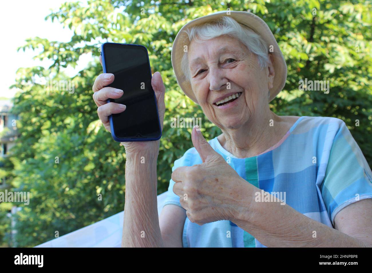 Joyeuse femme mûre montrant un téléphone isolé sur fond de nature Banque D'Images