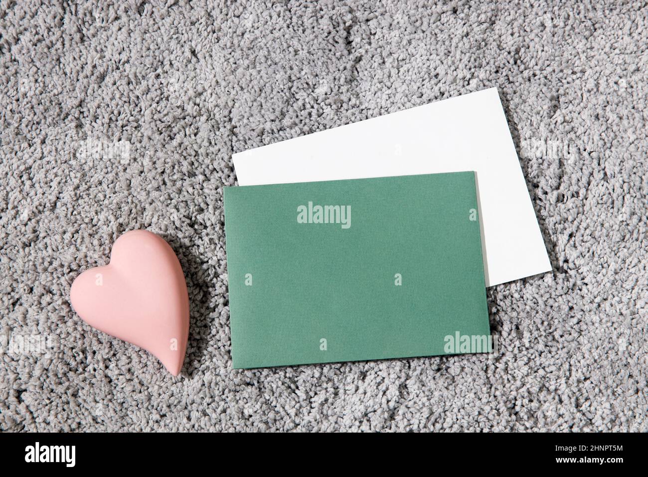 Carte de vœux pour la Saint-Valentin. Enveloppes blanches et vertes, coeur rose en céramique sur fond de moquette gris. Copier l'espace. Placer pour le texte Banque D'Images