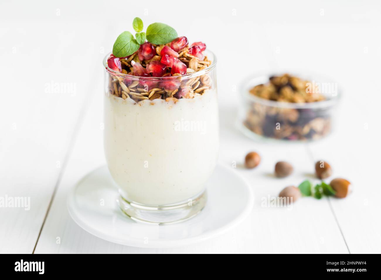 Petit-déjeuner sain concept. Crème fraîche vanille avec granola dans un verre garni de grenadier et menthe disposées sur une table en bois blanc. Banque D'Images