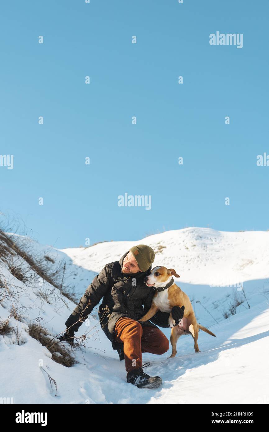 Un homme heureux et son chien espiègle s'amusent dans la neige au soleil Banque D'Images