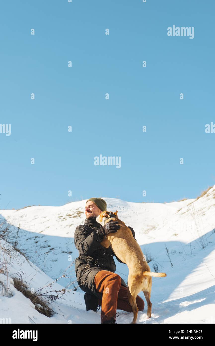 Un homme heureux et son chien espiègle s'amusent dans la neige au soleil Banque D'Images