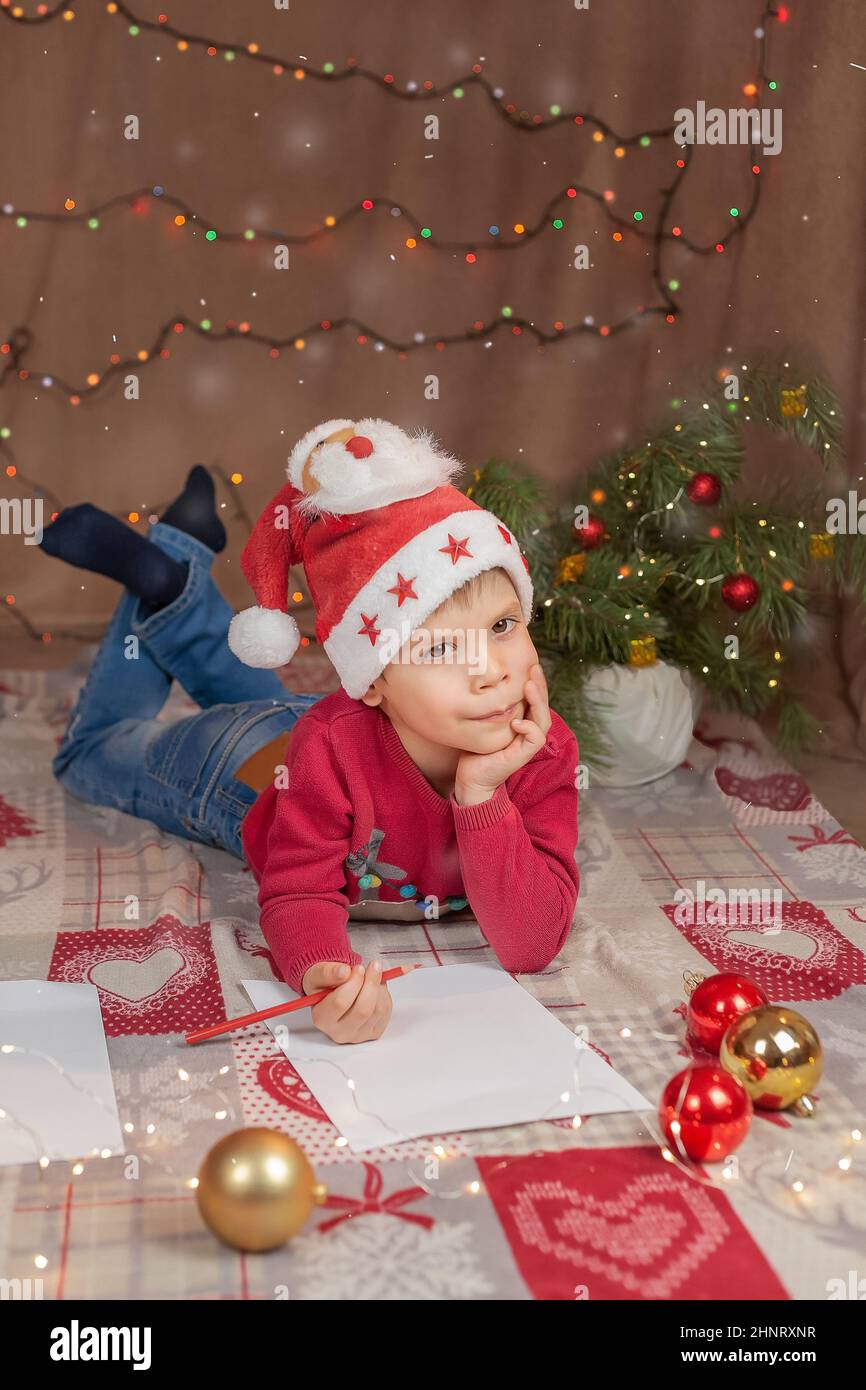 Un garçon de Noël écrit une lettre au Père Noël. Lettre d'aide de Noël pour enfant en chapeau rouge Banque D'Images