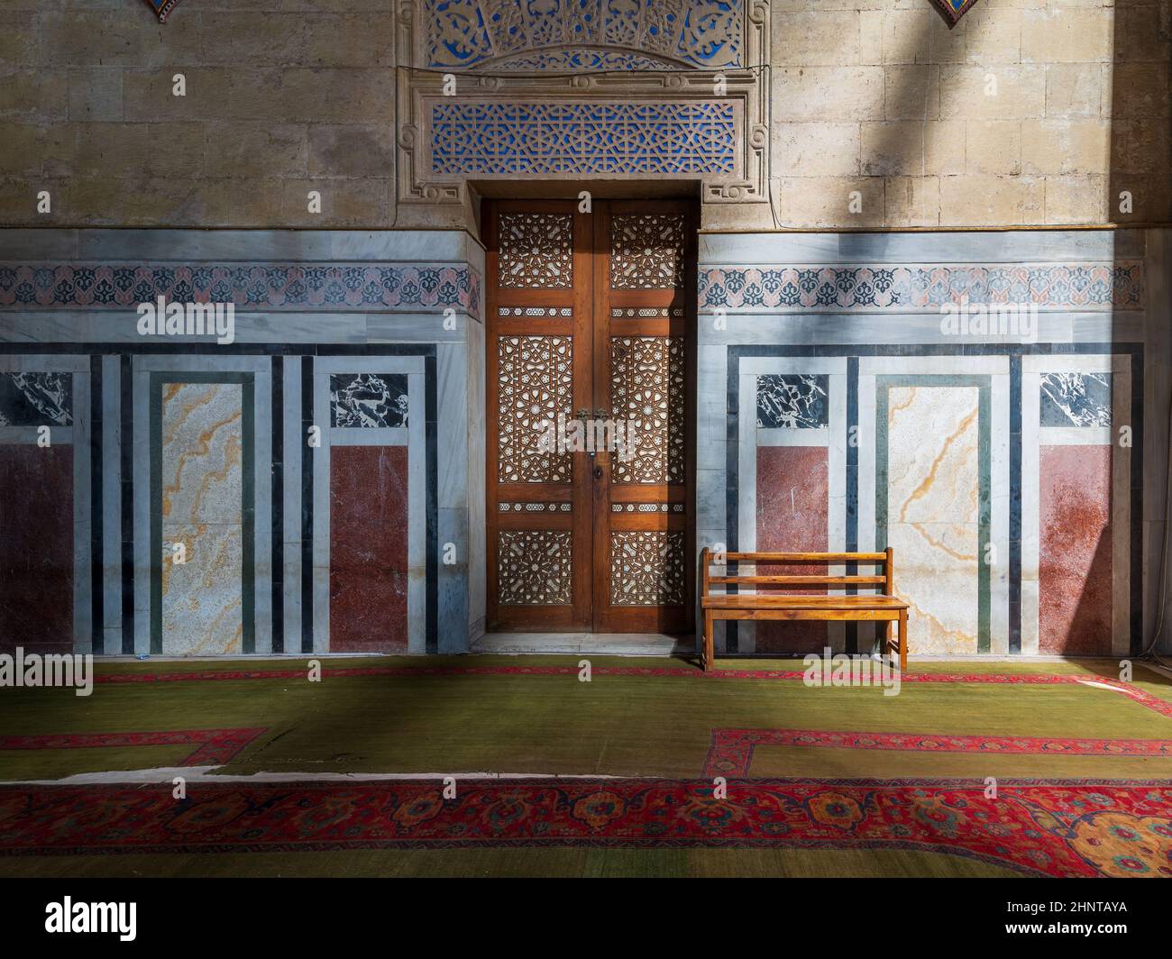 Porte en bois ornementale, murs décorés de mosaïques, banc en bois et sol éclairé par des poutres apparentes, mosquée Al Rifai, le Caire, Égypte Banque D'Images