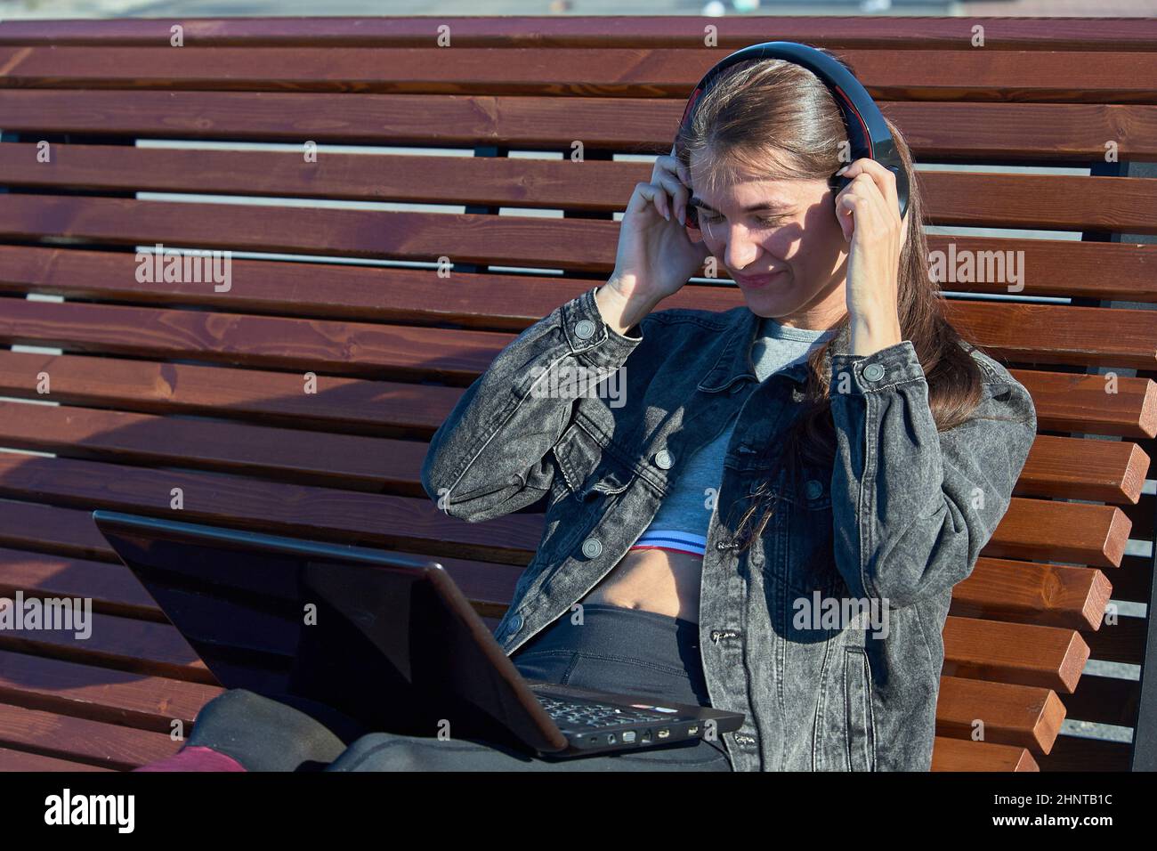 Une femme avec un ordinateur portable est assise sur un banc de rue et écoute de la musique avec des écouteurs Banque D'Images