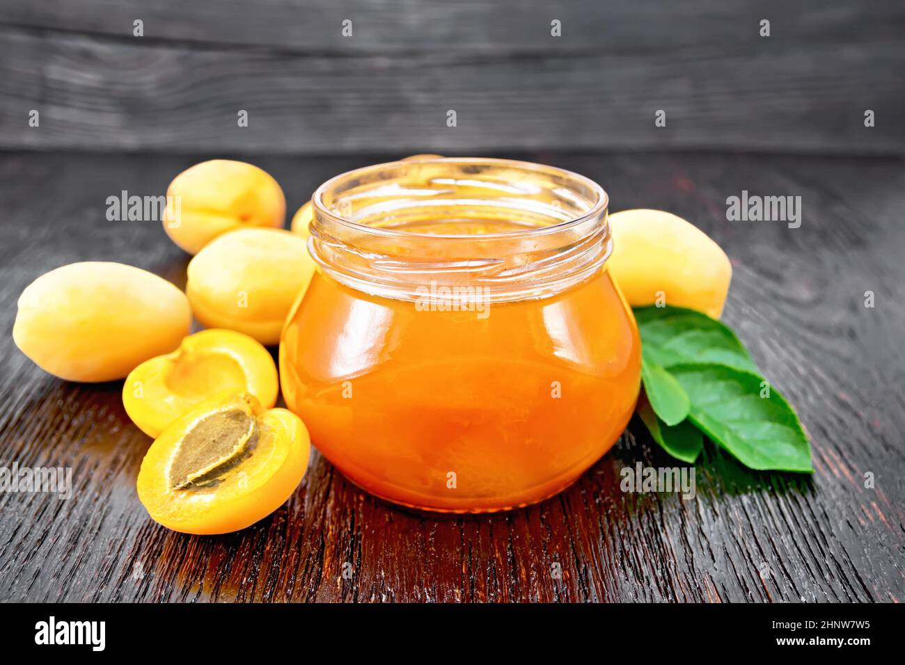 Confiture d'abricot dans un pot en verre, fruits et une branche avec des feuilles vertes sur le fond de bois foncé Banque D'Images