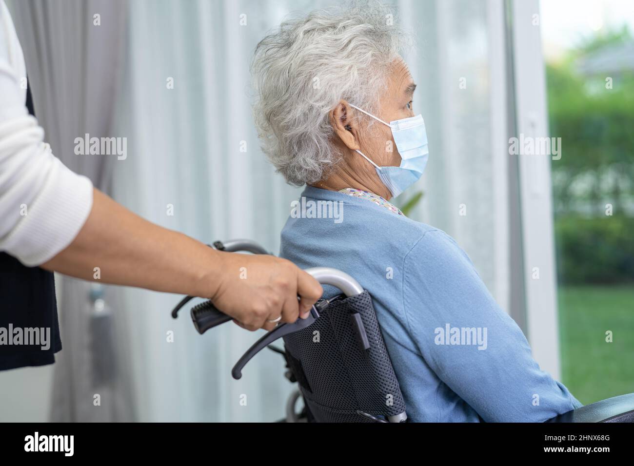 Aidez la vieille femme asiatique âgée assise sur un fauteuil roulant et portant un masque facial pour protéger l'infection à Covid-19 coronavirus. Banque D'Images