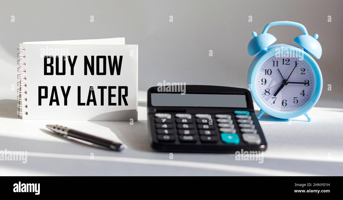 Sur une table blanche se trouve une calculatrice, un stylo et un bloc-notes avec l'inscription ACHETER MAINTENANT PAYER PLUS TARD. Banque D'Images