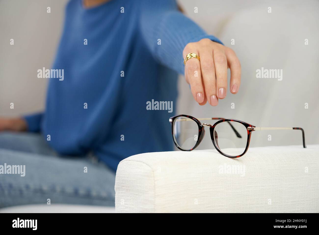Problème de vue. Femme atteignant pour des lunettes sur le canapé, ayant une mauvaise vue des yeux. Banque D'Images