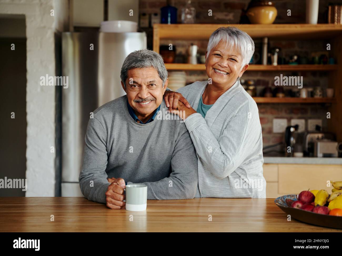 Portrait d'un couple biracial âgé à la retraite heureux debout, souriant à l'appareil photo dans leur cuisine moderne. Banque D'Images