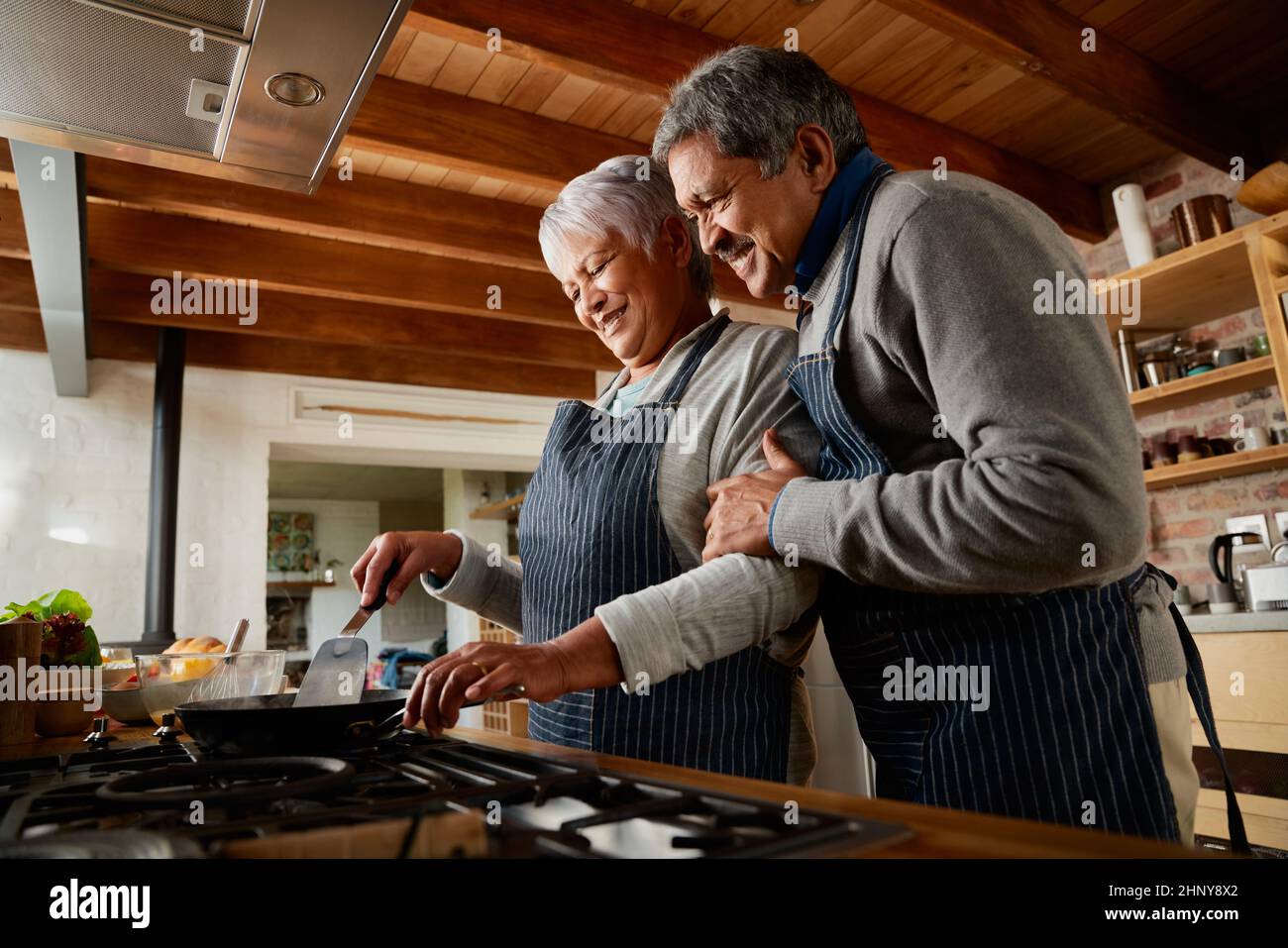 Couple multiethnique âgé souriant tout en cuisinant ensemble dans leur cuisine moderne. Heureux et en bonne santé à la retraite Banque D'Images