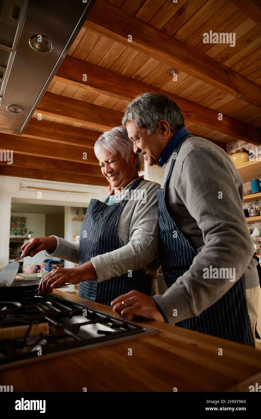 Orientation portrait d'un couple multiethnique âgé cuisant le petit déjeuner ensemble dans leur cuisine moderne. Banque D'Images