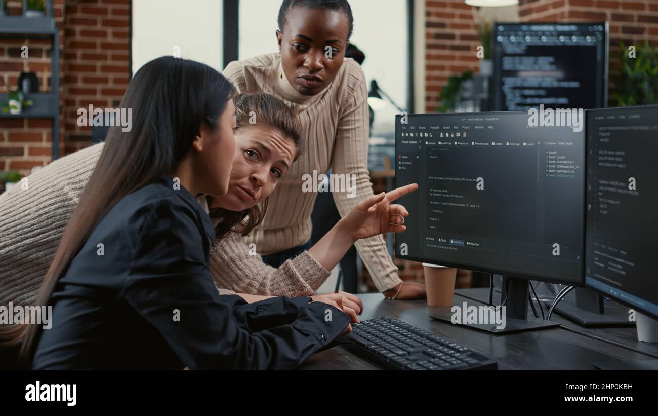 Le programme pointant vers l'écran d'ordinateur expliquant le code en cours d'exécution à des collègues brainstorming des idées de logiciel dans l'agence indépendante. Équipe mixte d'ingénieurs logiciels collaborant sur le projet du groupe informatique. Banque D'Images