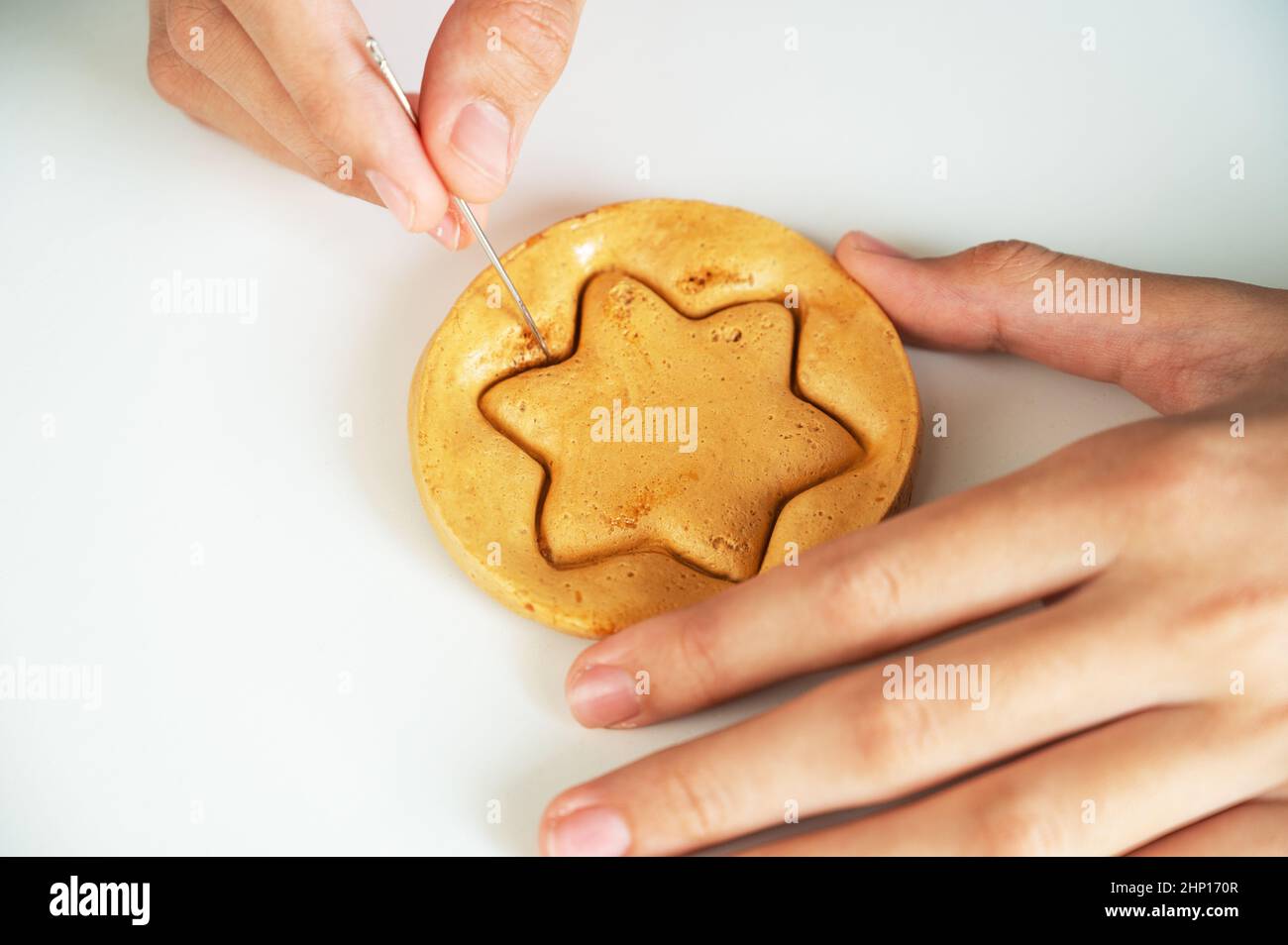 Les mains de gros plan scratch cassent sucre caramel bonbons biscuits avec une aiguille en métal en forme d'étoile sur un fond blanc. Banque D'Images