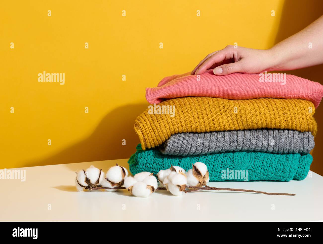 femme tenant une pile de chandails tricotés pliés sur un fond jaune.Laver les vêtements, nettoyer les choses Banque D'Images
