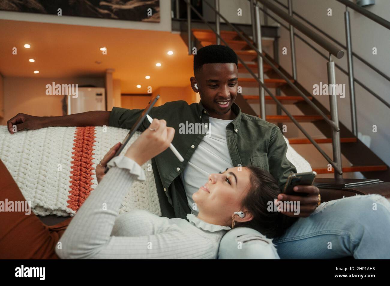 Couple biracial assis sur un canapé à l'aide de la technologie Banque D'Images